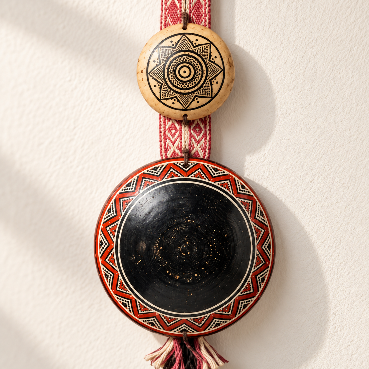 Dúo Colgante Ceremonial en Tutuma y Disco Negro con Cinta Tejida · detalle de la superficie; ambientación digital a partir de la imagen de catálogo. Elementos del escenario no incluidos.