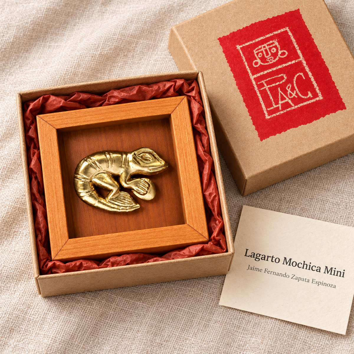 Lagarto Mochica Mini en caja de cartón microcorrugado con etiqueta PA&C y tarjeta específica de la obra; recreación digital de su presentación.